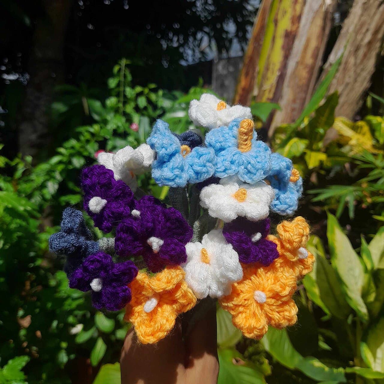 Close up of blue, purple, orange, and white crochet flowers gathered into a bouquet outdoors