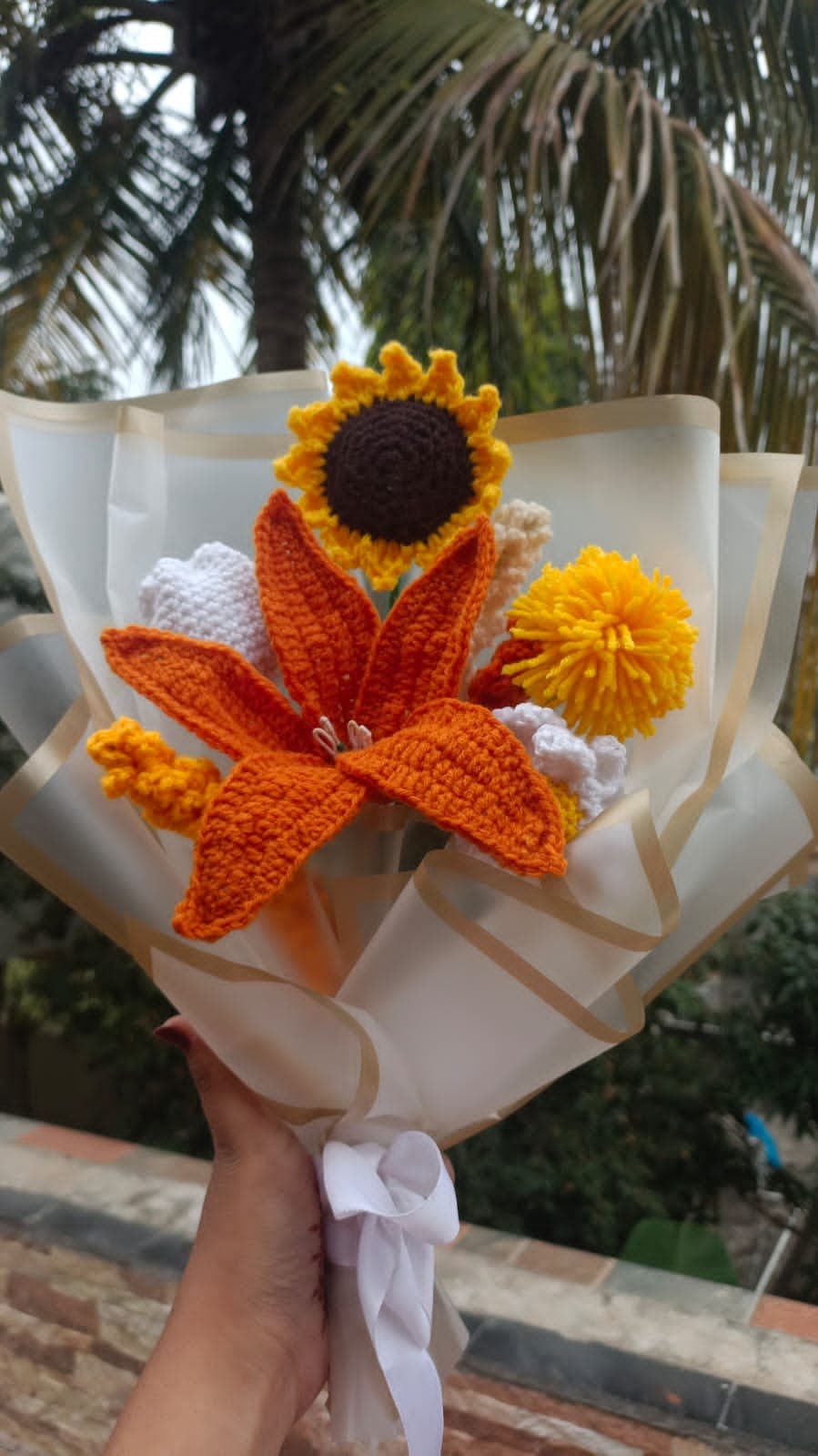 Tall crochet bouquet with an orange lily, yellow sunflower, and white blooms wrapped in white paper